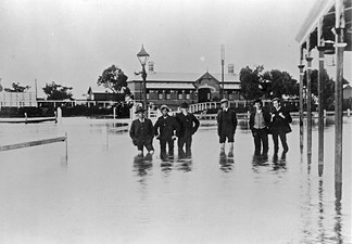 Men standing in floodwaters near the Railway Hotel and Warracknabeal Station, 23 August 1909