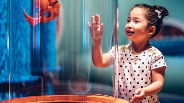 Girl laughing as she plays with the suction tube exhibit in the Ground Up exhibition at Scienceworks