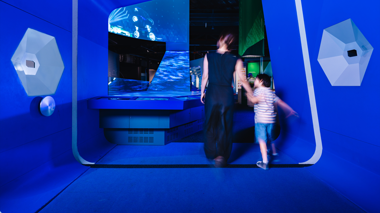An adult and child explore a blue-lit futuristic gallery space at Scienceworks.