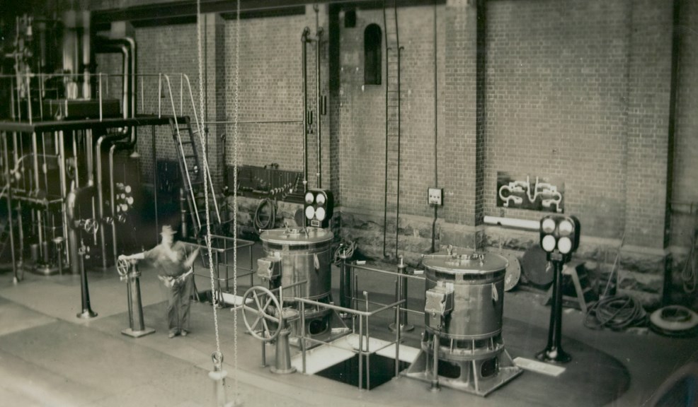 Overhead view looking down on the newly installed motors of electric pumps Nos. 10A & 10B in Well no. 10, North Engine Room, Spotswood Pumping Station, circa 1940. A worker stands beside the pumps leaning on the hydraulic inlet valve controls. Steam pumping engine No. 8 can be partially seen in the background.
