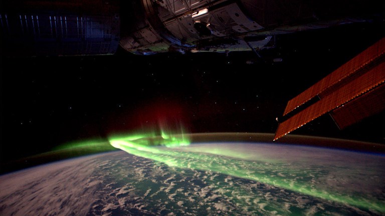 Looking down on the Earth from space with green glowing lights of the aurora.