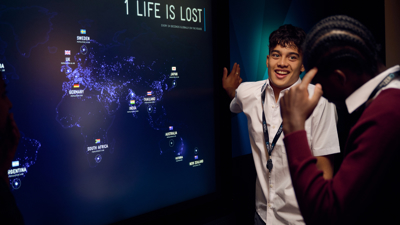 A student in the Road to Zero Experience Space standing in front of a touch screen with a map of the world on the screen 