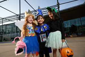 Three children in Halloween costumes carrying trick or treat baskets in the shape of pumpkins.