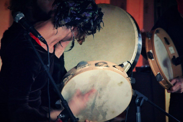 A musician with a feather earring plays the tambourine. 