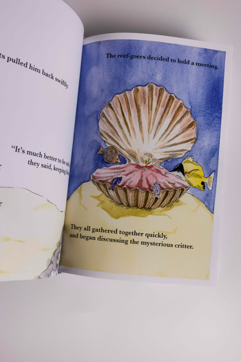 Open book displays an illustrated underwater scene with a large seashell surrounded by small fish. 
