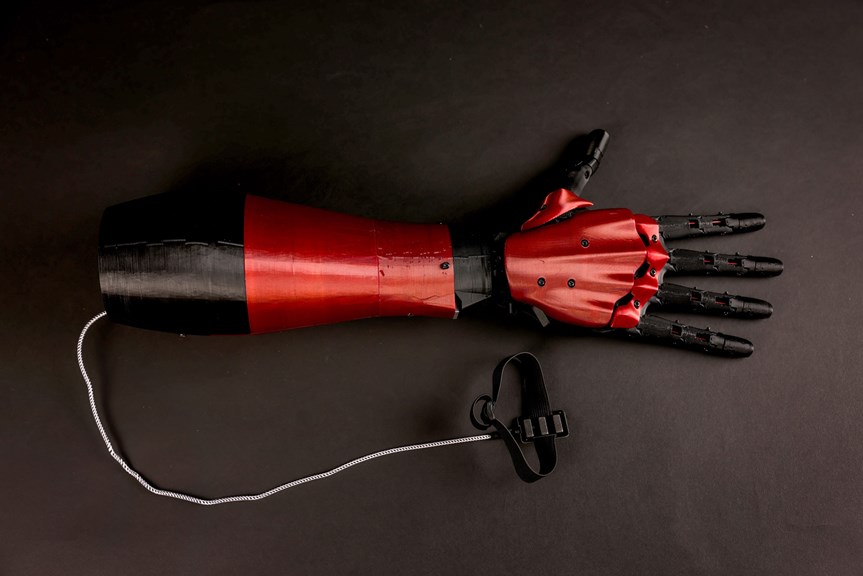 Red and black 3D printed prosthetic arm, with an attached cable and sensor.