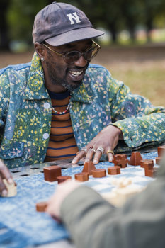 Maleik Njoroge smiles while playing chess with wooden pieces in the park.