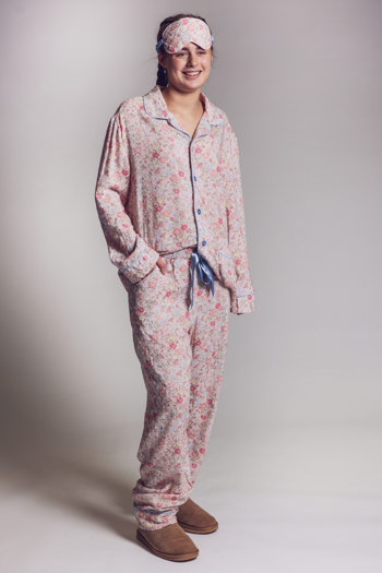 Model wearing pink floral pyjamas with matching sleep mask and blue piping detail, paired with tan slippers against a neutral background.