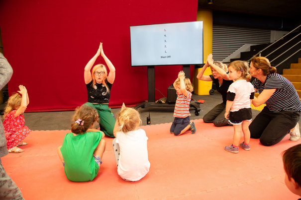 Staff member leading children in Moon Moves in the Amphitheatre, during Little Kids' Week In at Scienceworks