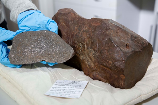 Blue gloved hands holding a grey rock next to a large brown rock on a conservation cushion