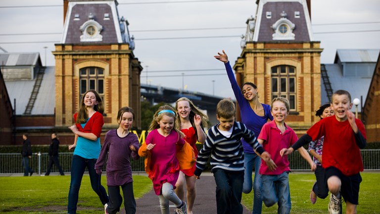 Group of children running towards the camera. Old brick building in the background