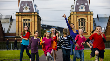 Group of children running towards the camera. Old brick building in the background