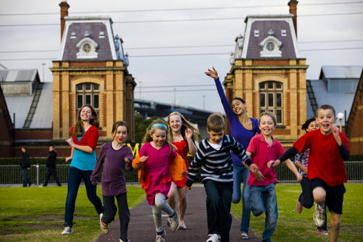 Group of children running towards the camera. Old brick building in the background