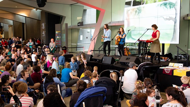 A large group of families with children sit and watch a musical act on stage