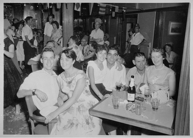 Men and women are arm in arm amid a table of drinks and a festive atmosphere. 