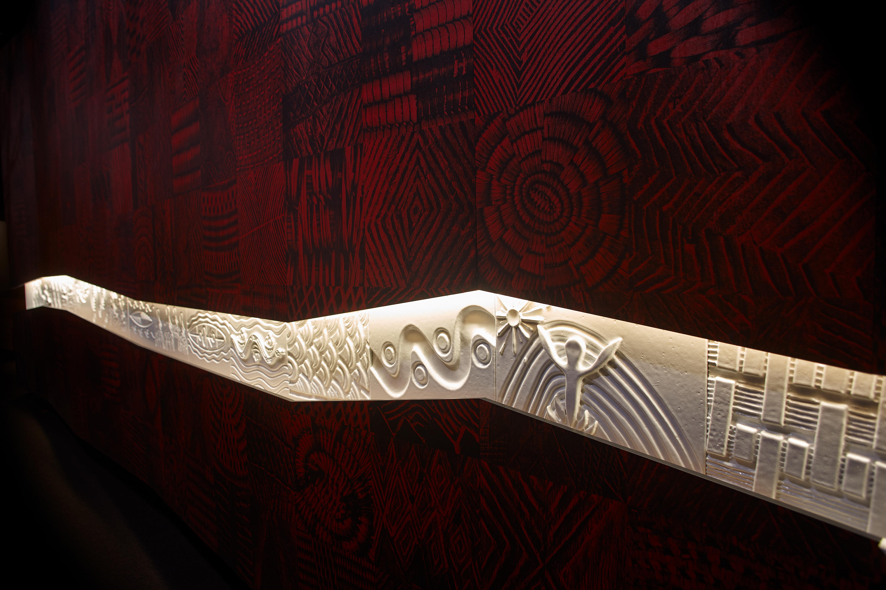 Several rectangular carved panels in a row against a red, patterned wall