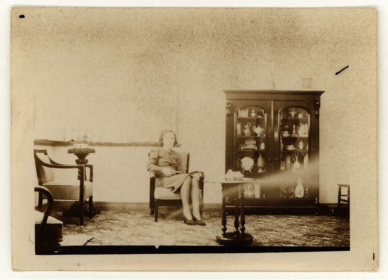 Ida Lilian Twycross' daughter Elizabeth McArthur at home in 1943. The display cabinet behind her is full of objects purchased at Melbourne International Exhibitions by her grandfather, John Twycross.