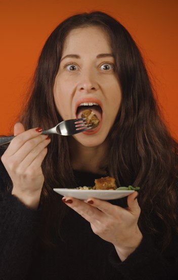 An apprehensive young woman is about to eat a mouthful of food. 