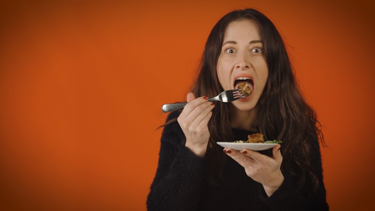 An apprehensive young woman is about to eat a mouthful of food. 