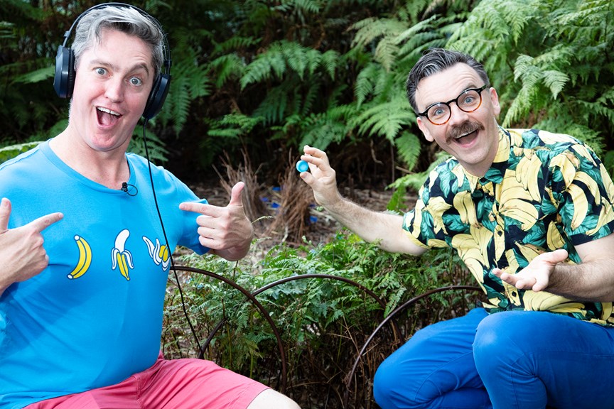 The Listies, comic duo Richard Higgins and Matt Kelly in Forest Gallery promoting their Melbourne Museum Audio Guide App. Matt is wearing headphones, Richard is holding blue bottle cap and pointing to Matt's blure t-shirt.
