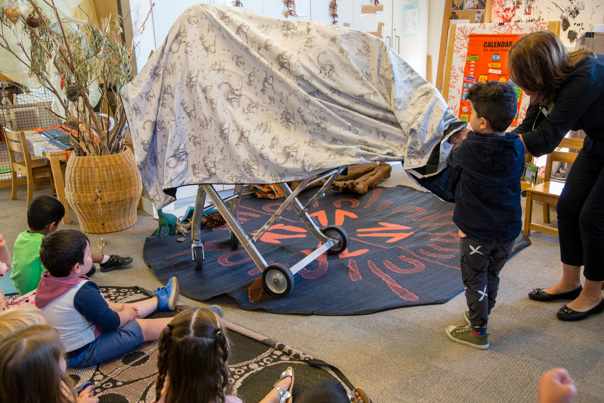 Kindergarten child helping Outreach Program Presenter,  to unveil the cast of a dinosaur bone during the Fossil program. 