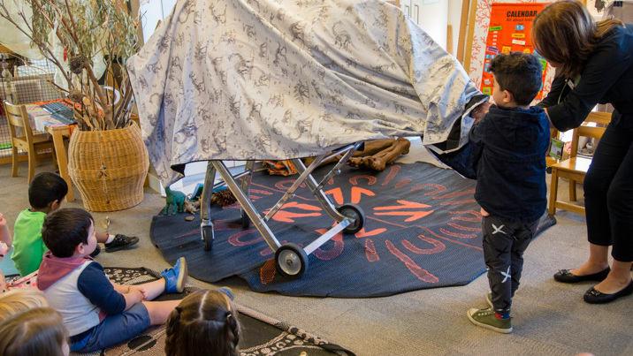 Kindergarten child helping Outreach Program Presenter,  to unveil the cast of a dinosaur bone during the Fossil program. 