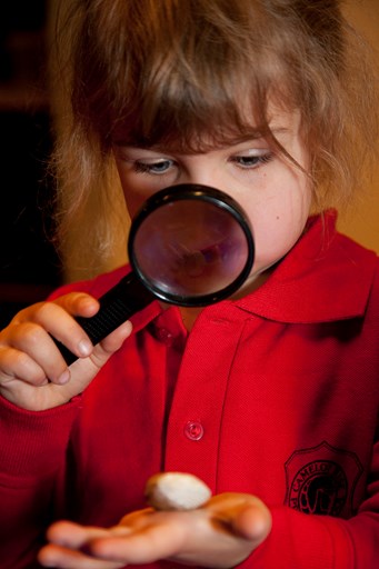 Child looking through a magnifying glass at an object on her palm