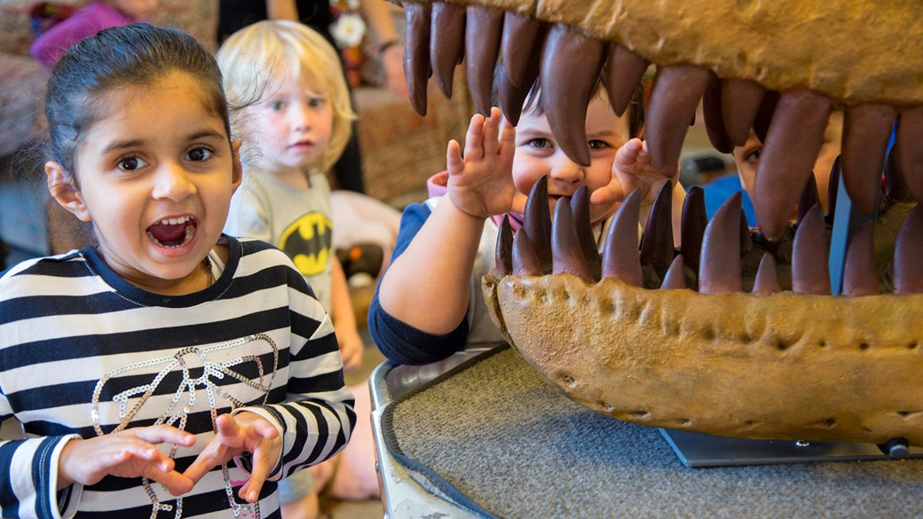 Children roaring next to a large model of a fossil dinosaur jaws.