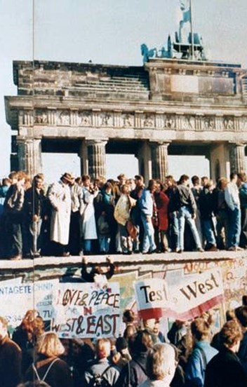 A crowd of people on top of a wall with a gate of stone columns behind them. 