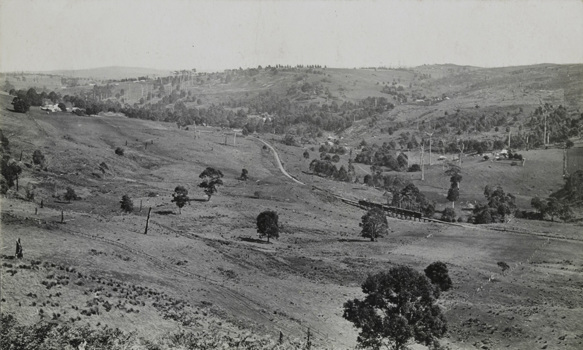 A steam locomotive hauling a train, crossing a small bridge