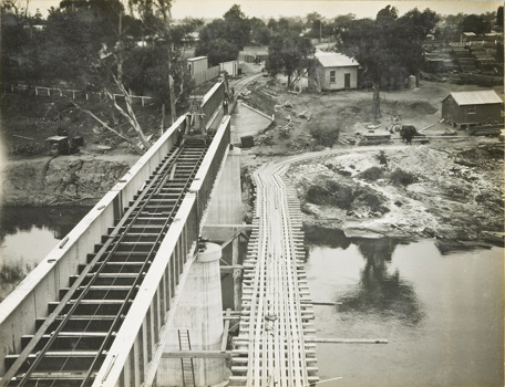 Constructing the rail bridge over the Murray River, Yarrawonga, circa 1930. The girder for the main spans is on the left and a temporary bridge with a construction tramway is on the right.