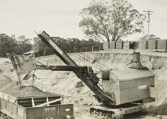 Construction of line, Yarrawonga, circa 1927-33. A Harman caterpillar-mounted steam shovel is loading ballast into rail trucks.