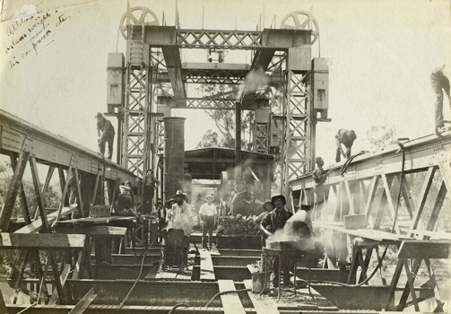 Staff constructing the bridge over the Murray River, on the Strathmerton to Tocumwal line, Tocumwal, 1906. Workers are hot-riveting strengthening plates along the top chord of the span truss using portable forges and pneumatic riveting guns.