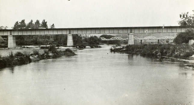 The Tambo River bridge, of riveted steel girder construction on concrete piers, as seen from the river, on the Bairnsdale to Orbost line, 1914. A five span timber truss road bridge is visible in the background.