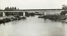 The Tambo River bridge, of riveted steel girder construction on concrete piers, as seen from the river, on the Bairnsdale to Orbost line, 1914. A five span timber truss road bridge is visible in the background.