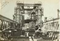 Staff constructing the bridge over the Murray River on the Strathmerton to Tocumwal line, Tocumwal, 1906. Workers are hot-riveting strengthening plates along the top chord of the span truss using portable forges and pneumatic riveting guns.