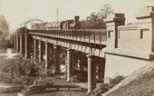 A steam engine with a combination of goods, livestock and passenger carriages crossing a long bridge at Echuca, prior to 9 June 1906