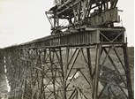 A travelling crane is on top of one of the towers of the Maribyrnong River Viaduct on the Albion to Broadmeadows line, Keilor East, 1928. A girder, awaiting placement, is sitting on a cradle beneath it.