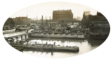 Spencer Street Bridge, circa 1917-30. The north pier is in the foreground with the north abutment behind. A temporary bridge on the left links the two. There are boats moored further left. In the background are the Administrative Offices of the Victorian Railways.