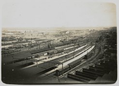 Spencer Street Station, post-1910. Covered railway platforms and railway yards. A large number of goods carriages in background. Passenger carriages near covered platforms. Railway line has been electrified.