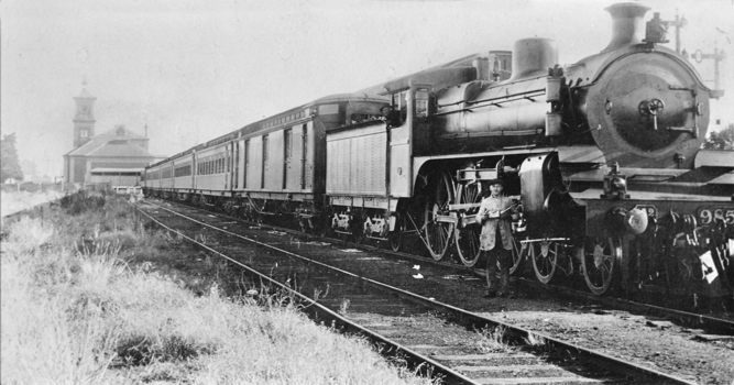 Staff member beside A2 class steam locomotive no. 985 hauling passenger carriages, circa 1930