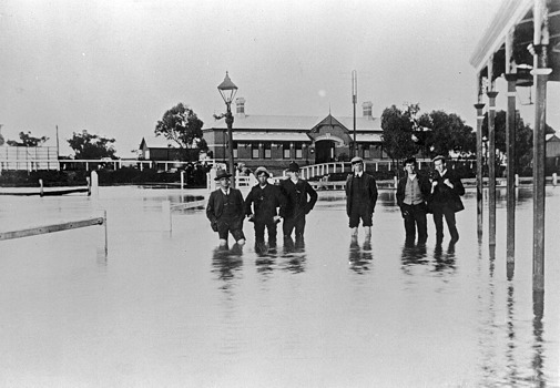 Men standing in floodwaters near the Railway Hotel and Warracknabeal Station, 23 August 1909