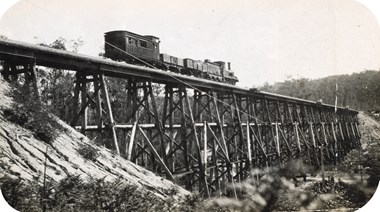 An R class steam locomotive and tender drawing two trucks and a guard's van over the completed Stony Creek Bridge, on the Bairnsdale to Orbost line, circa 1915