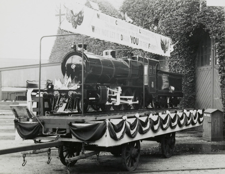 Railway-themed military recruitment display, Victoria, circa 1930. A model train stands on a flatbed truck. The train, which is decorated, carries a sign reading "Model of consolidation locomotive, the most powerful in the Commonwealth. Why not let it draw you to the front?"
