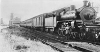 Staff member beside A2 class steam locomotive no. 985 hauling passenger carriages, circa 1930