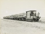 Two men standing on the front of the petrol-powered Fordson rail motor which is hauling eight trucks with a weight of 200 tons (204 tonnes) on the Yarrawonga to Oaklands line, Yarrawonga, circa 1930