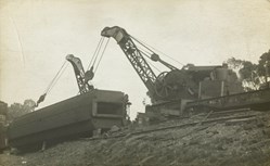 Two large cranes attempting to right an overturned railway carriage by means of cables around the carriage, circa 1910