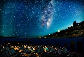 People sitting in theatre recliner chairs looking at a projection of the night sky