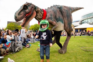 Boy wearing a dinosaur mask standing in front of a dinosaur puppet