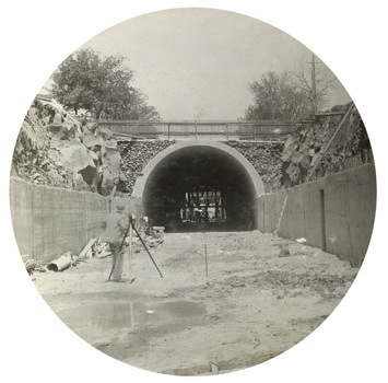 Tunnel construction on the South Kensington to West Footscray line, Footscray, 1928. A man with a theodolite stands in front of a tunnel.